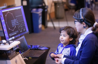 A mother and small child are looking at a computer screen